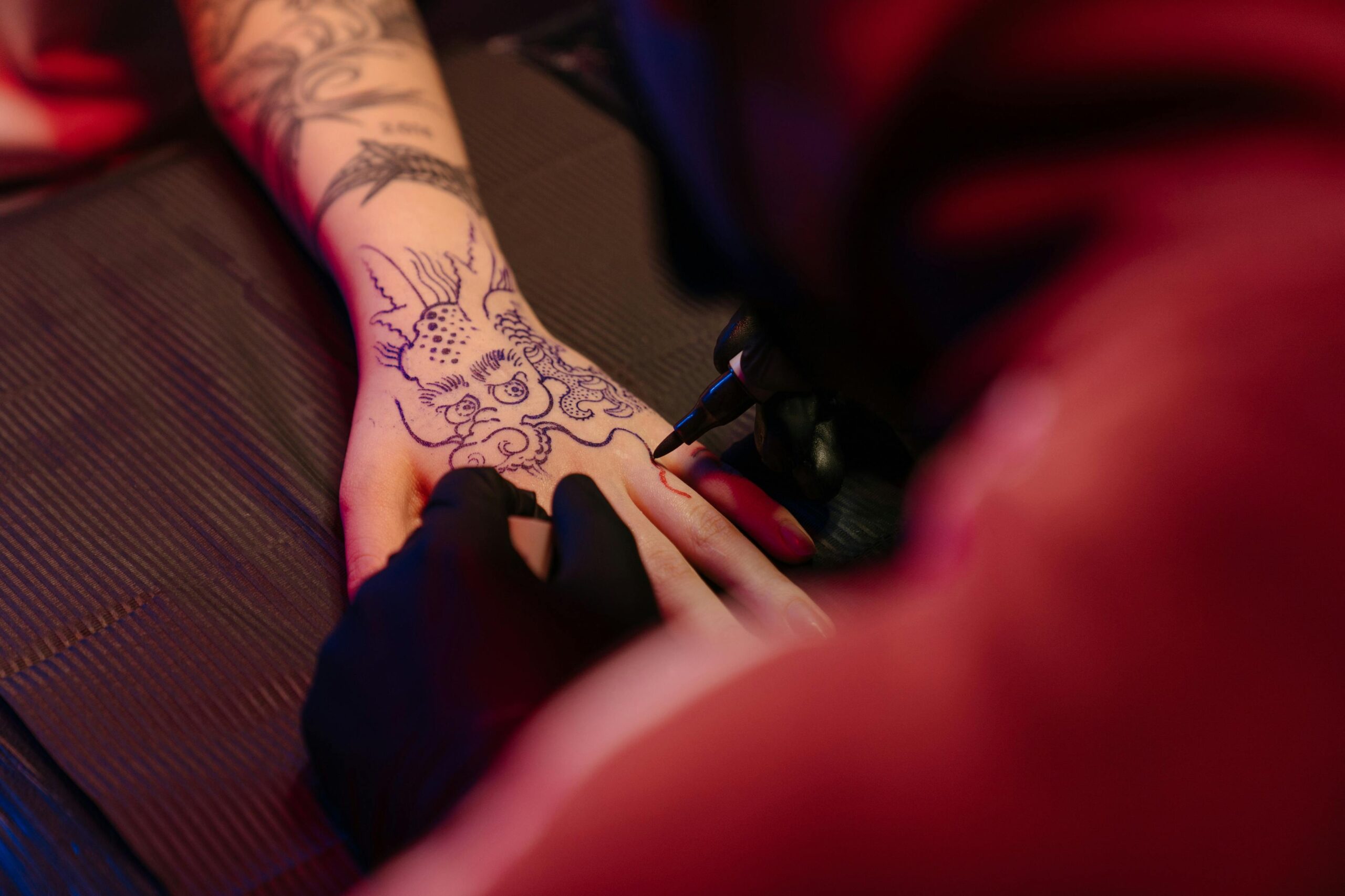 Close-up of a tattoo artist in action, creating a unique dragon tattoo on a client's hand under neon light.